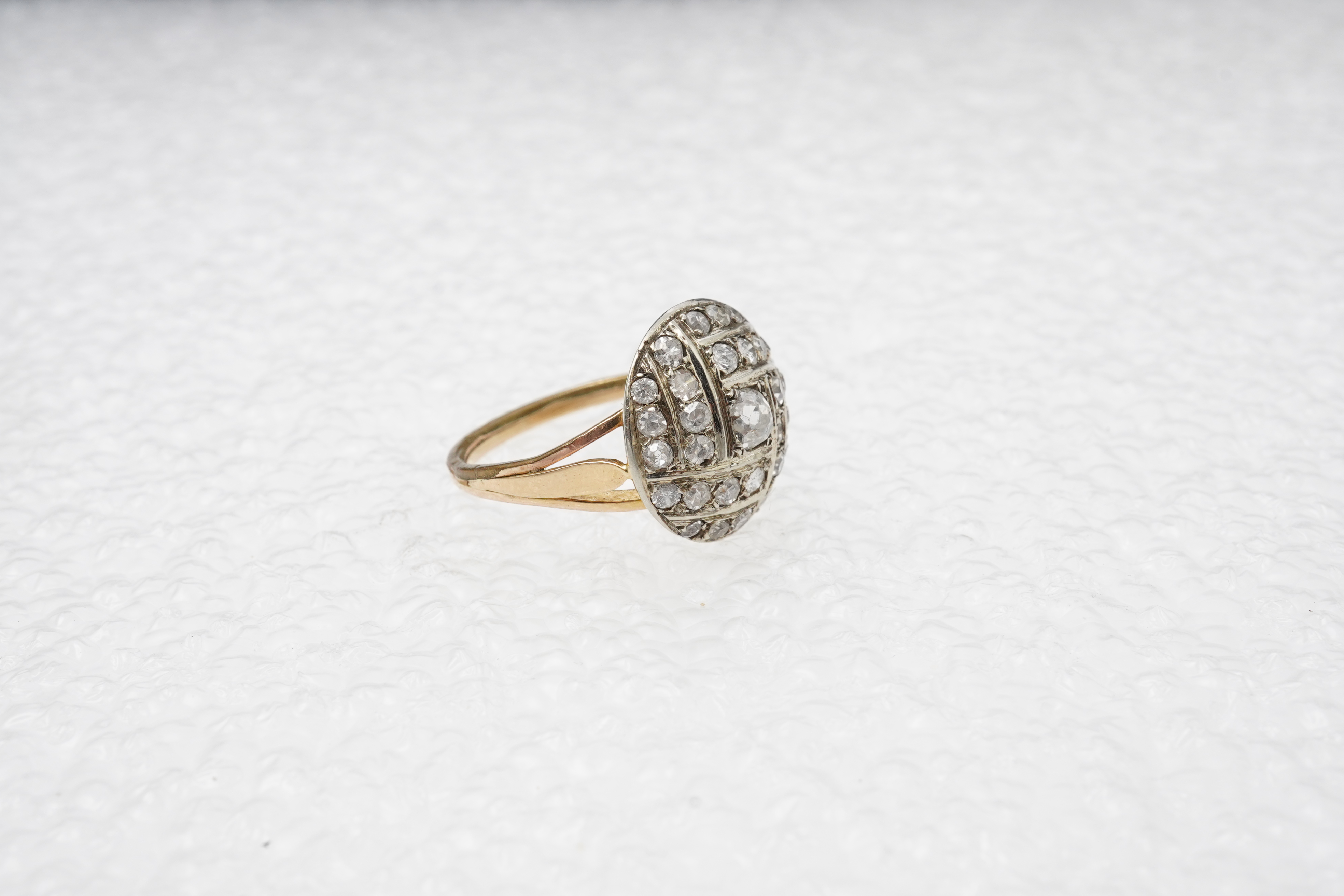 A diamond ring, centring on a circular motif of bombé design, set with geometric arrangements of cushion-shaped, single- and circular-cut diamonds totalling approximately 0.90 carats, to a gold band, size M1/2, indistinc